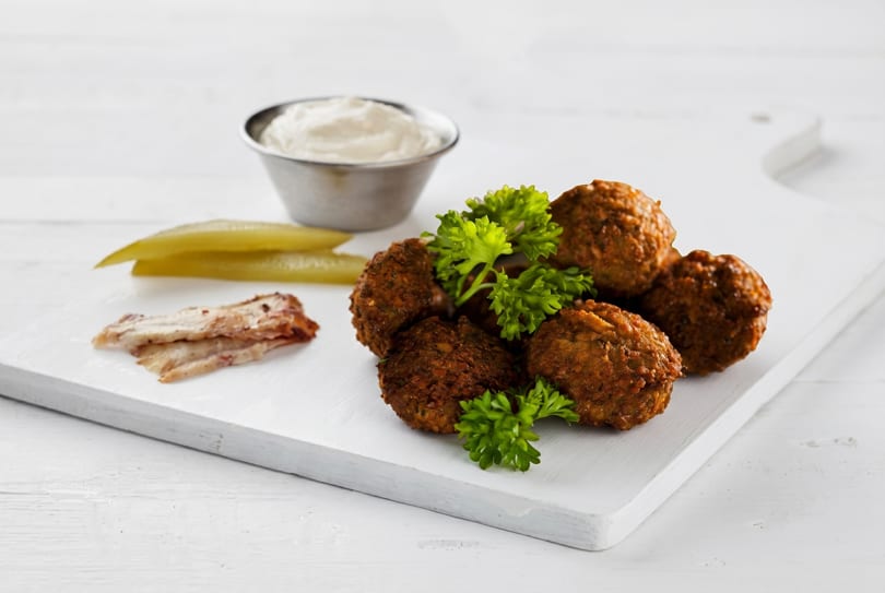 Falafel balls with parsley, pickles, and a side of white sauce on a white cutting board.